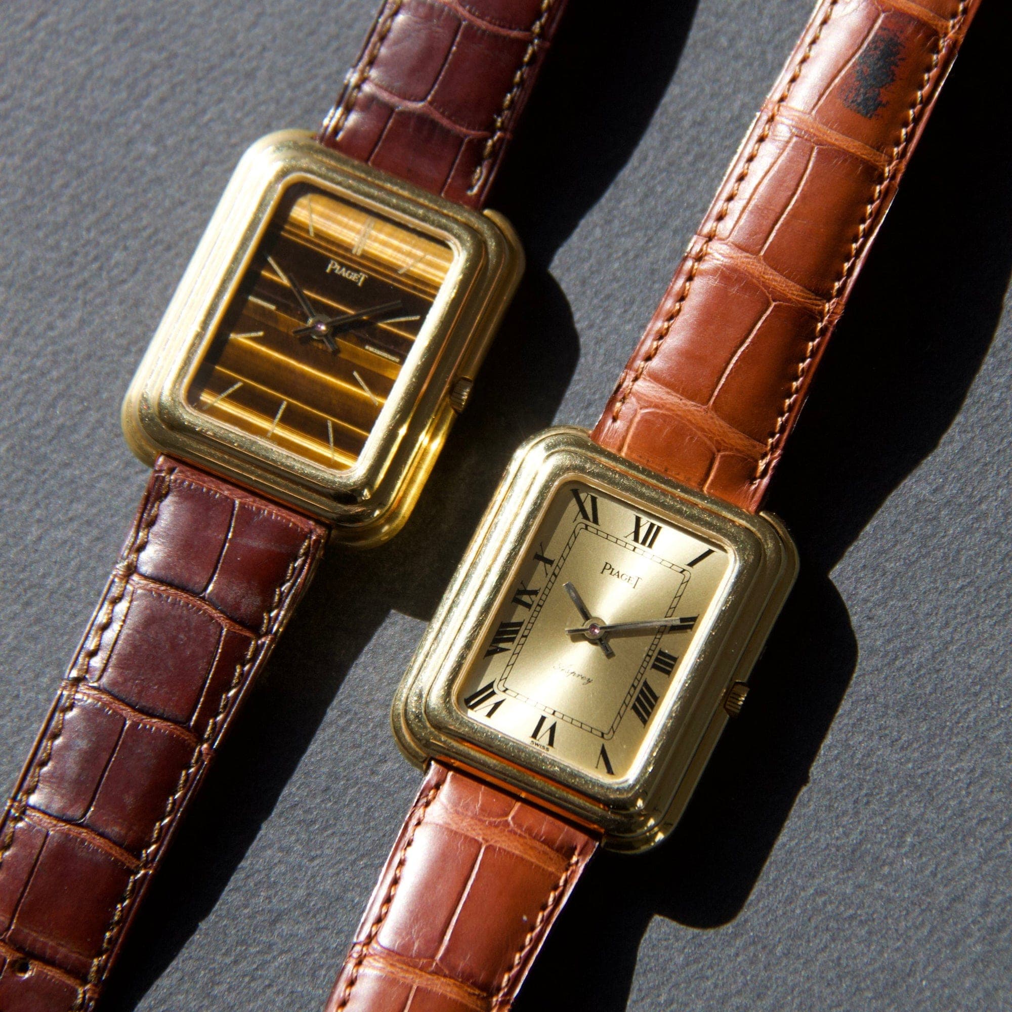 Two vintage Piaget watches with rectangular yellow gold cases on brown leather straps, one with a tiger's eye dial and one with a champagne Roman-numeral dial